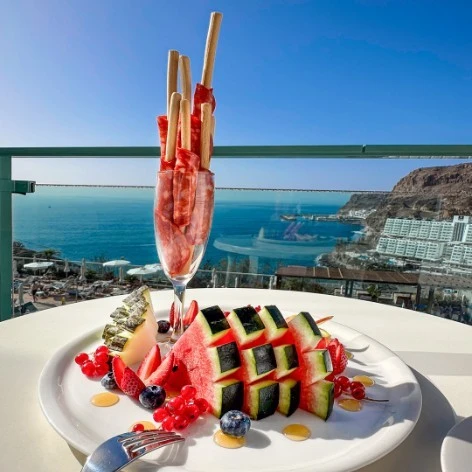 Plato de fruta con sand&iacute;a y verduras, vista al mar desde un balc&oacute;n