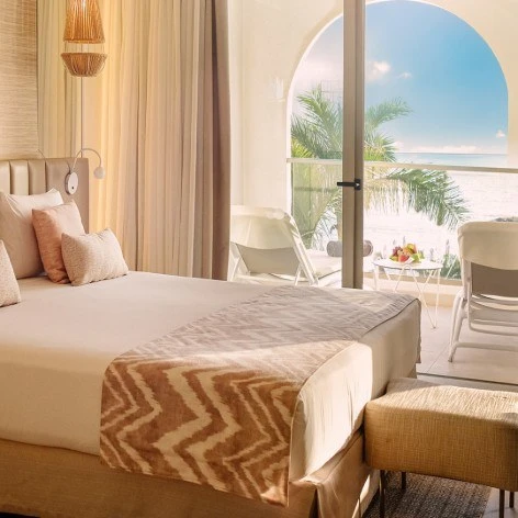 Dormitorio con cama y luz natural junto a terraza con vista al mar.