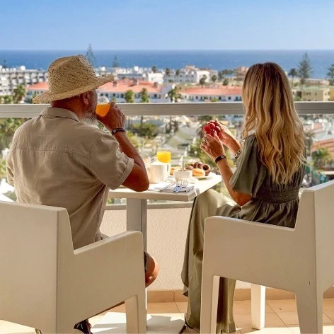 Pareja brindando y comiendo en terraza con vista al mar y ciudad