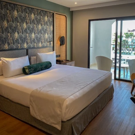 Dormitorio moderno con cama doble, pared decorada y salida a balc&oacute;n.