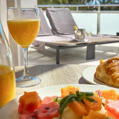 Copa de jugo y croissant con desayuno frente a ventana.