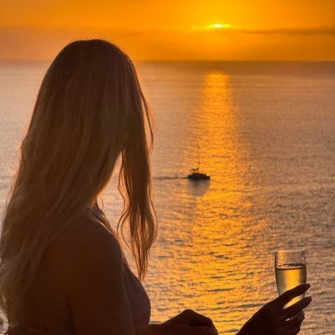 Mujer en la playa al atardecer, mirando el mar con una copa en la mano