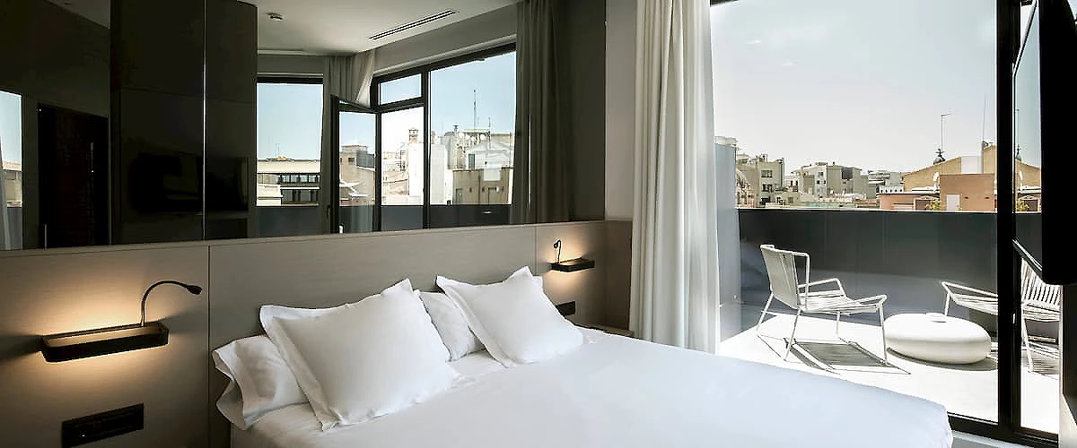 Habitaci&oacute;n moderna con cama blanca y balc&oacute;n con vistas urbanas