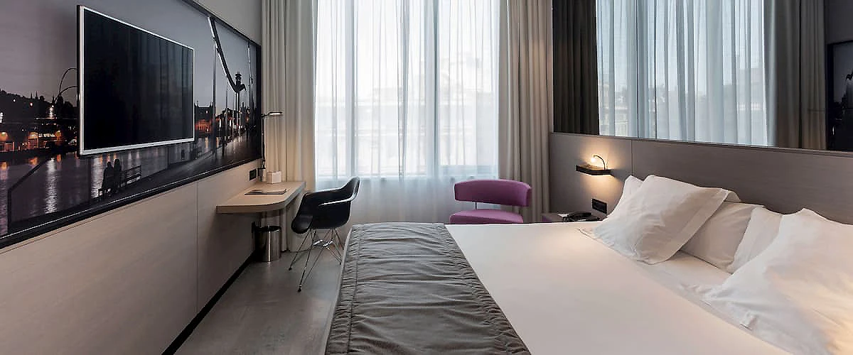Habitaci&oacute;n de hotel moderna con cama doble y grandes ventanales al atardecer