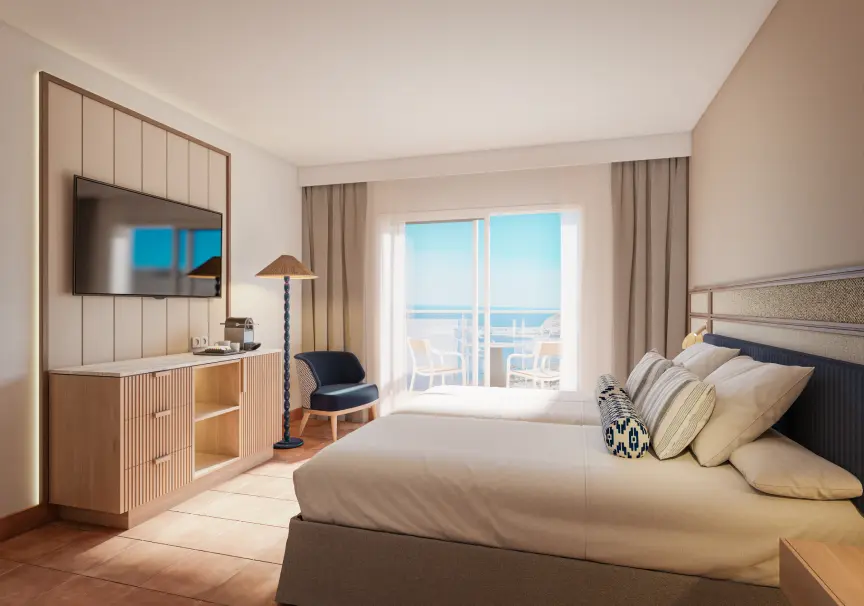 Habitaci&oacute;n de hotel moderna con cama, televisor y balc&oacute;n con vista al mar.