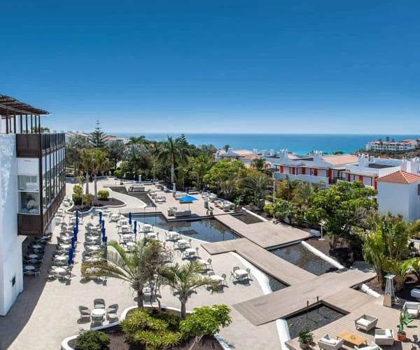 Vista panor&aacute;mica de un hotel con piscina y palmeras frente al mar