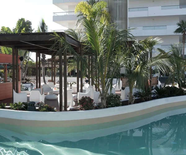 Piscina con palmeras y camastros junto a un hotel moderno