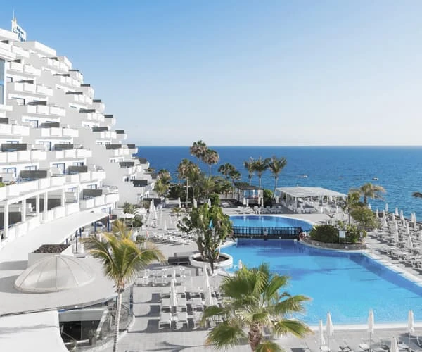 Hotel con piscina y vistas al mar desde un balc&oacute;n, con palmeras