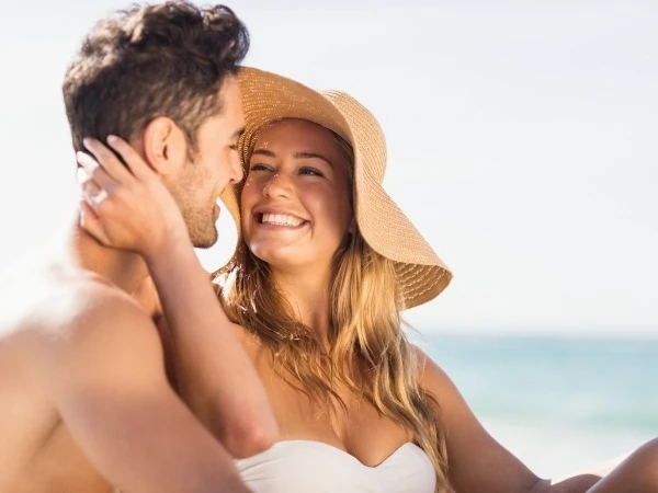 Pareja de vacaciones en la playa, ella sonr&iacute;e con sombrero de paja