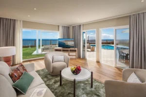 Sala luminosa con sof&aacute;, mesa y vista al mar desde ventanas corredizas