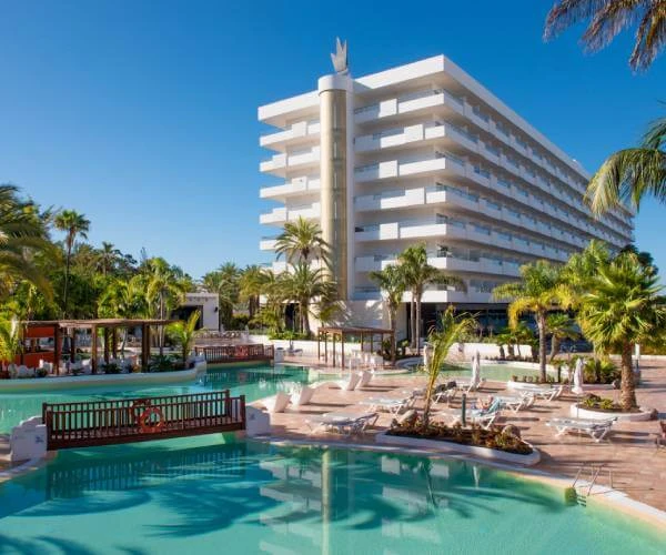 Hotel moderno blanco con piscina y palmeras bajo cielo azul