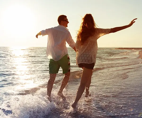 Pareja caminando juntos por la orilla del mar al atardecer, salpicando agua