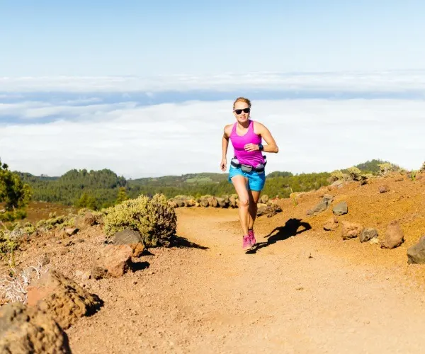 Mujer corriendo en sendero de monta&ntilde;a con cielo despejado