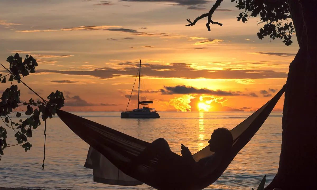Hamac en la playa con una puesta de sol y un velero al fondo (&le;80)