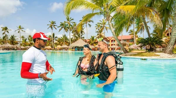 Pareja y gu&iacute;a con trajes de buceo en piscina tropical junto a palmeras