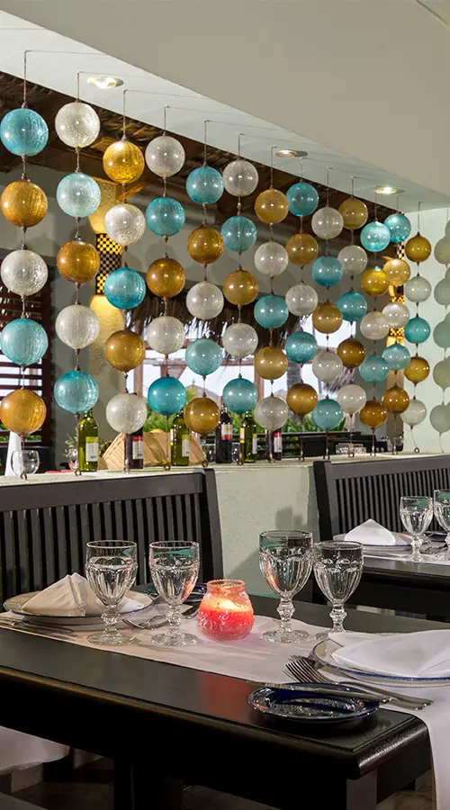 Mesa con velas y copas, y decoraci&oacute;n colgante de esferas de colores en evento.