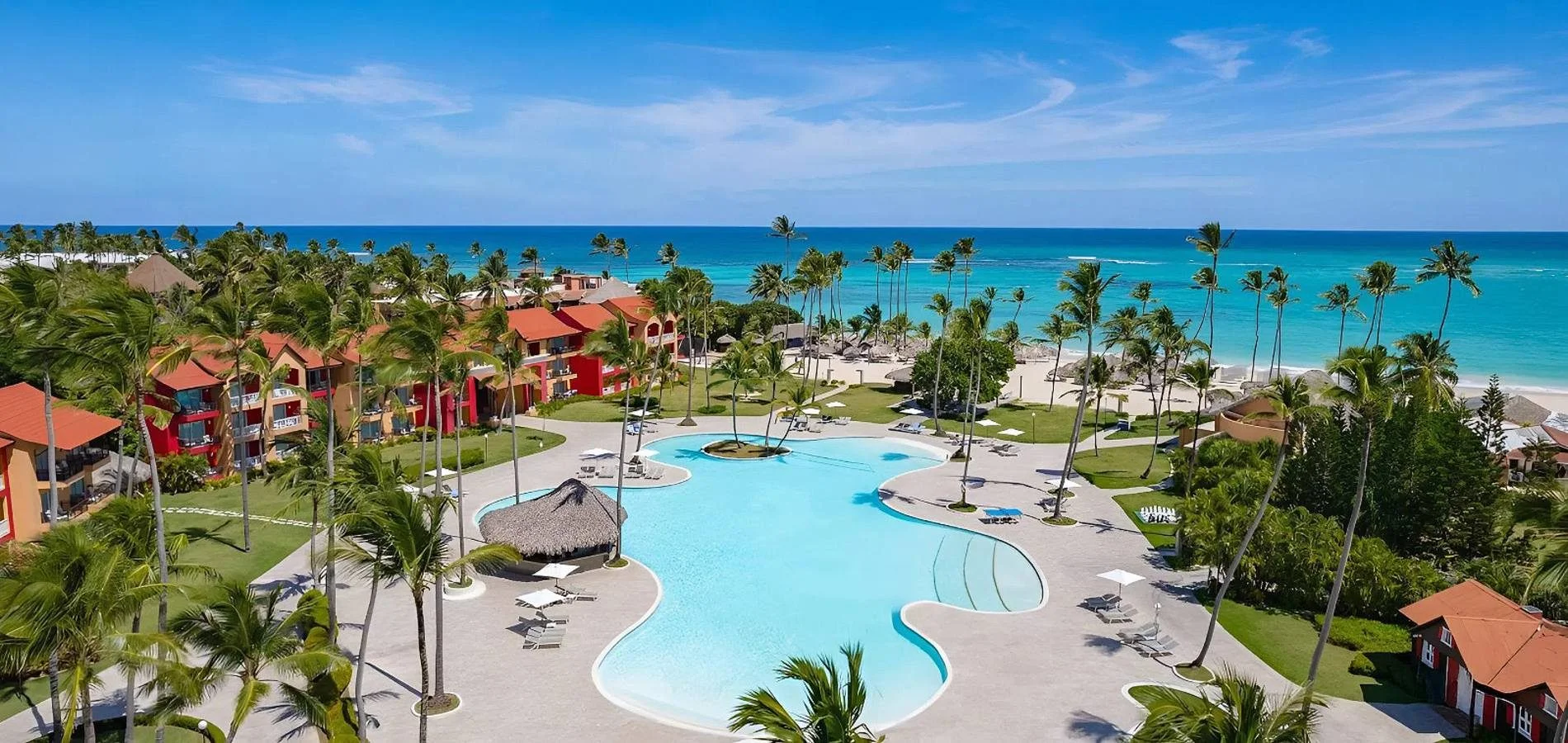 Hotel junto al mar con piscina, palmeras y edificios de colores.