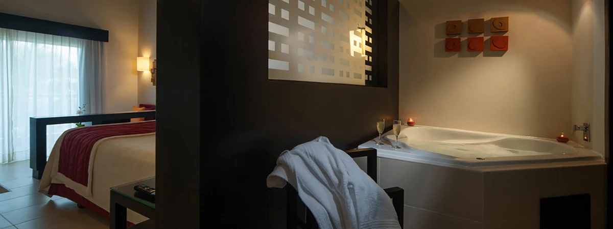 Habitaci&oacute;n de hotel con cama, cortinas y jacuzzi con dos copas iluminadas