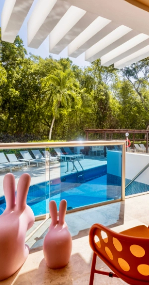 Piscina con palmeras y techo blanco, vista desde terraza con sillas.
