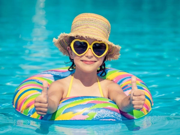 Ni&ntilde;a en piscina con gorro y gafas amarillas, pulgares arriba.