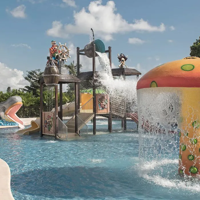 Parque acu&aacute;tico con surtidor de agua y tobog&aacute;n naranja bajo cielo azul