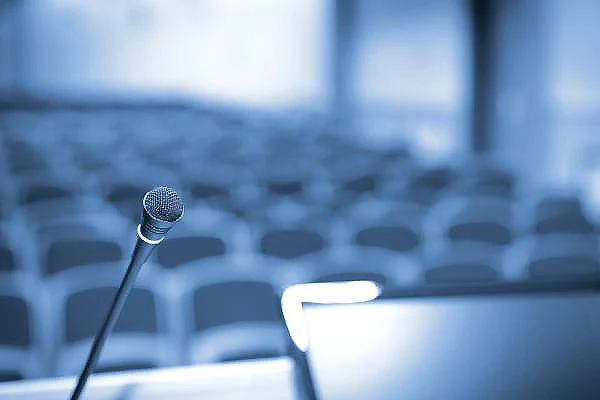 Micr&oacute;fono sobre un atril en un auditorio con sillas desenfocadas al fondo