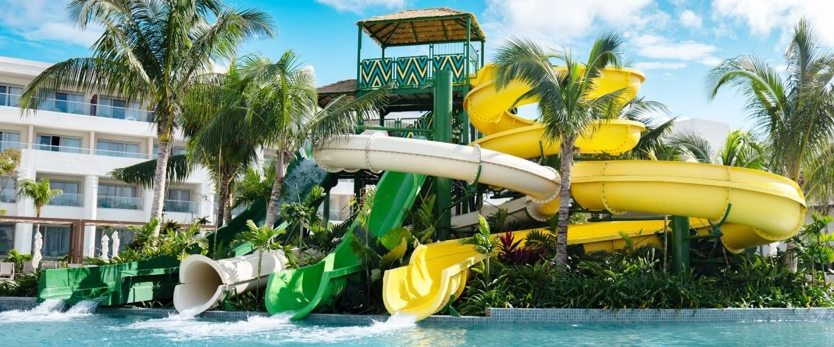 Toboganes acu&aacute;ticos amarillos y verdes junto a palmeras en un hotel tropical