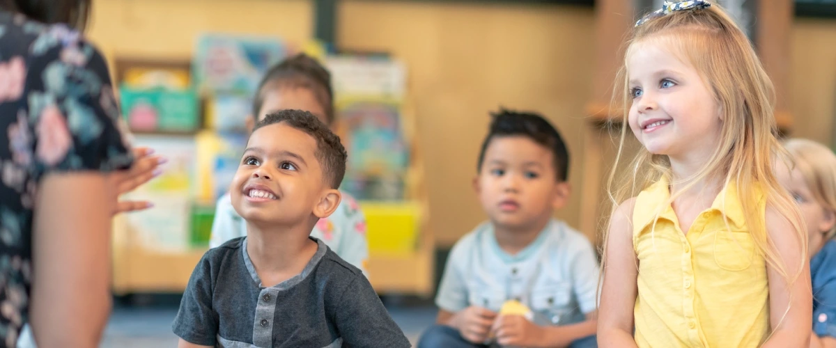 Ni&ntilde;a y ni&ntilde;o sonrientes en un aula, con otros ni&ntilde;os al fondo.