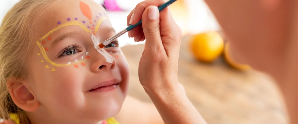 Ni&ntilde;a con maquillaje facial, pintando con pincel cerca de los ojos