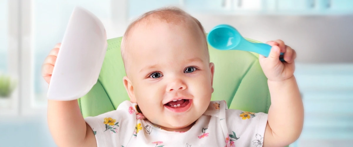 Beb&eacute; sonriente sostiene una esponja y un cepillo en la ducha.