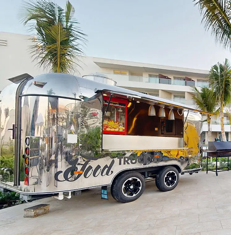 Autob&uacute;s tur&iacute;stico blanco &ldquo;Truck Cool&rdquo; con palmeras y hotel al fondo.