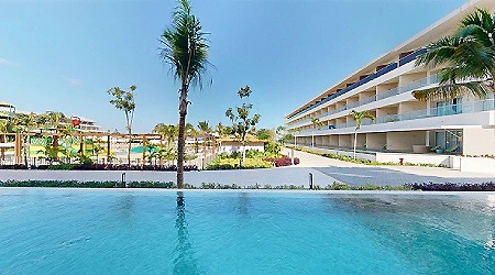 Piscina al aire libre con palmeras y edificio frente al mar
