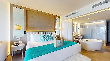 Habitaci&oacute;n moderna con cama, cortinas y ba&ntilde;era en suite hotelera.