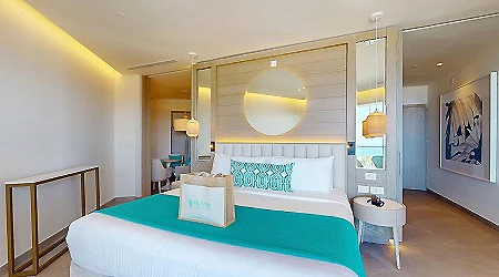 Habitaci&oacute;n de hotel con cama azul y verde, ventana y l&aacute;mparas colgantes