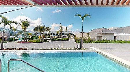 Piscina exterior con palmeras y jard&iacute;n, bajo cielo despejado.