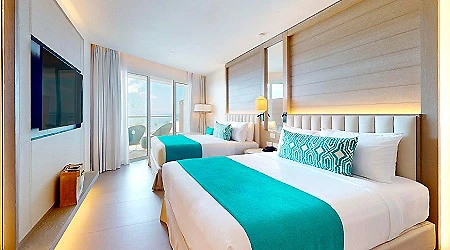 Habitaci&oacute;n de hotel moderna con cama doble y tonos turquesa y blanco.