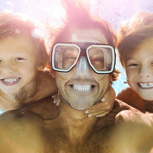 Bajo el agua, un hombre con gafas de buceo sonr&iacute;e entre dos ni&ntilde;os felices.