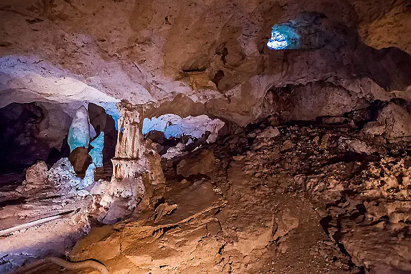 Cueva subterr&aacute;nea con rocas y escombros, luz azul en el fondo.