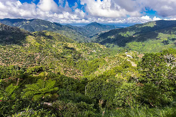 Paisaje monta&ntilde;oso verde con valles, nubes y cielo azul sobre el bosque