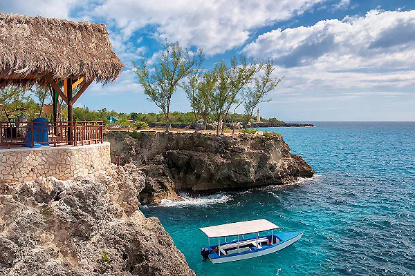 Barca azul junto a acantilados y caba&ntilde;as con techo de paja frente al mar
