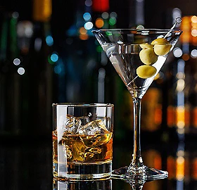 C&oacute;ctel en copa con aceitunas y bebida dorada en vaso sobre fondo borroso