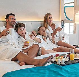 Familia en pijama desayunando juntos en la cama, ri&eacute;ndose y brindando
