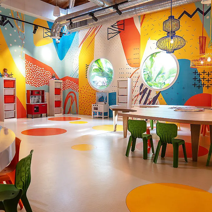 Aula infantil colorida con mesas, sillas y globos colgantes decorativos.