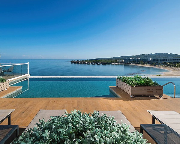Vista de la piscina y la bah&iacute;a con costa y colinas al fondo.