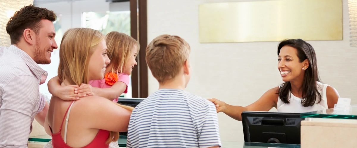 Familia sonriente en recepci&oacute;n; madre atiende a ni&ntilde;o y padre observa