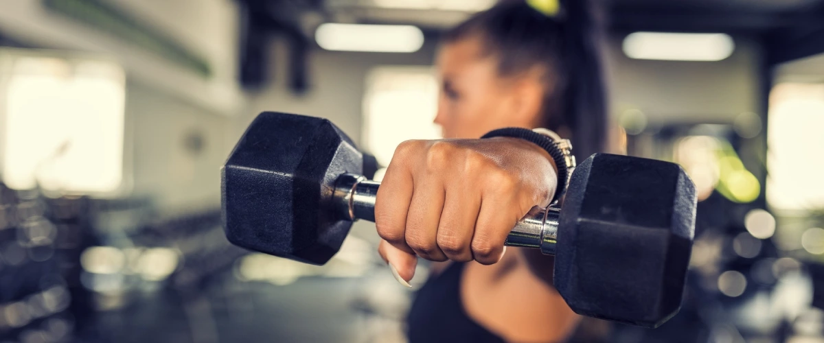 Persona entrenando con mancuernas en un gimnasio, sosteniendo una pesada.