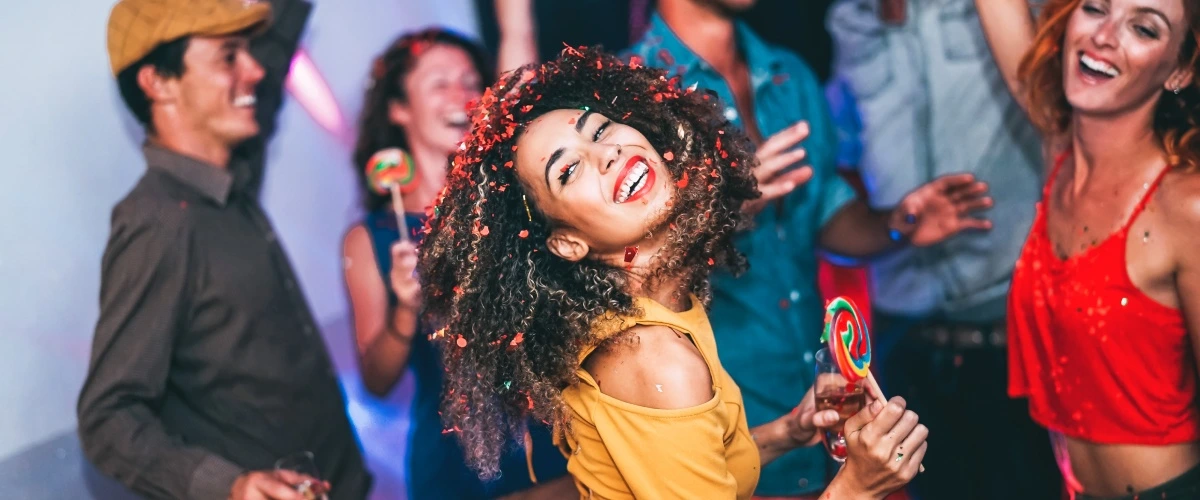 Mujer con cabello rizado y confeti sonr&iacute;e en fiesta con amigos.