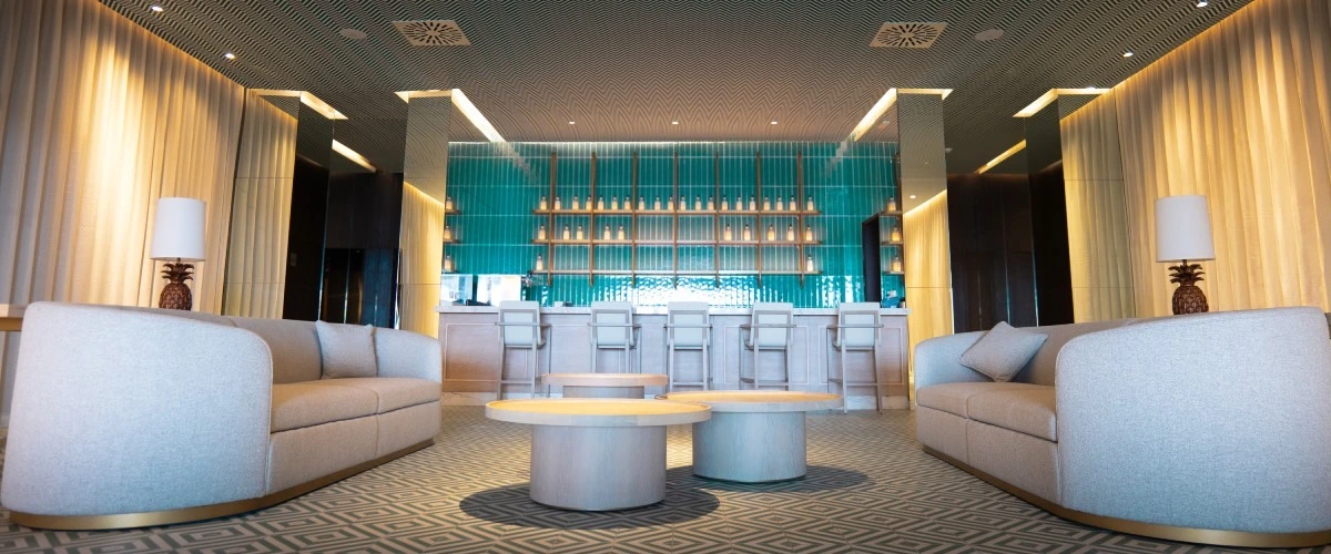 Lobby moderno con mostrador, iluminaci&oacute;n tenue y sof&aacute;s grises en ambos lados