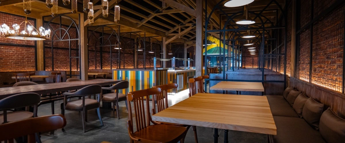 Interior de pub con mesas de madera, sof&aacute;s y techo de vigas con l&aacute;mparas.