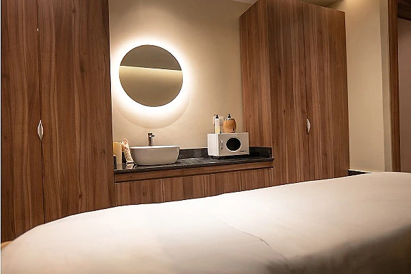 Lavabo moderno en ba&ntilde;o con muebles de madera y espejo circular.